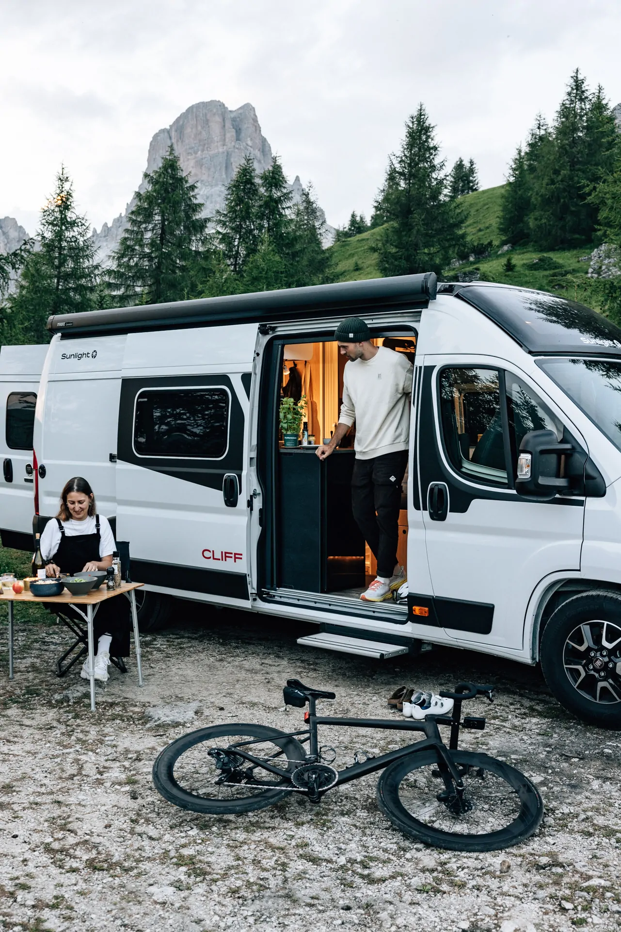 Compact white campervan parked in nature with open side door and bicycle in front, ready for an outdoor road trip in Sardinia.